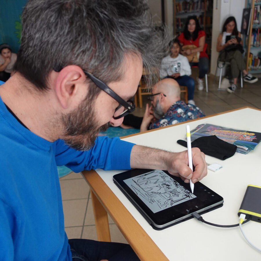 L'artista Andrea Scopetta disegna su un iPad una storia creata insieme ai bambini. Sullo sfondo il pubblico.